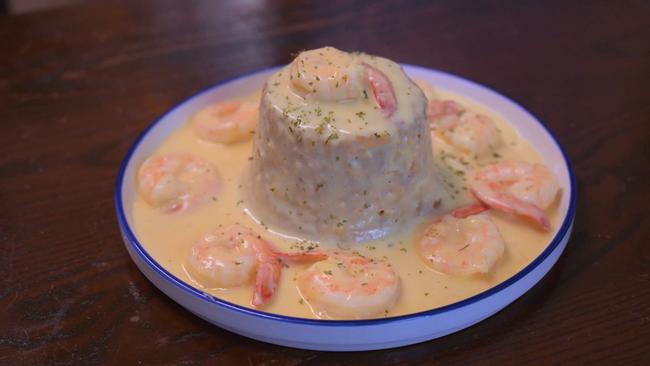 Cinematic high angle shot of a traditional Puerto Rican mofongo dish. Mashed green plantains served with succulent shrimp and sauce on a white ceramic plate