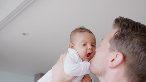 loving father lifting 3 month old baby daughter in the air in kitchen at home