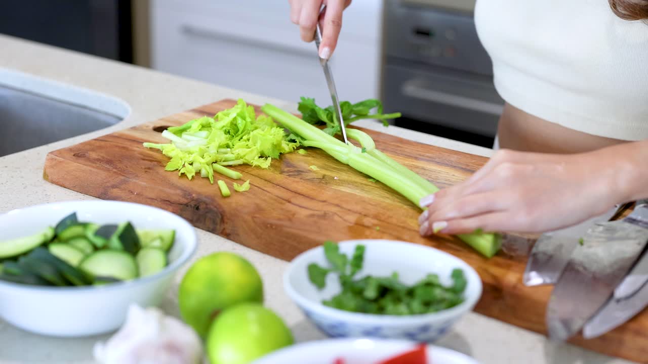 Hands slicing celery on a wooden board in a bright kitchen. Fresh ingredients and natural lighting create a clean, inviting atmosphere