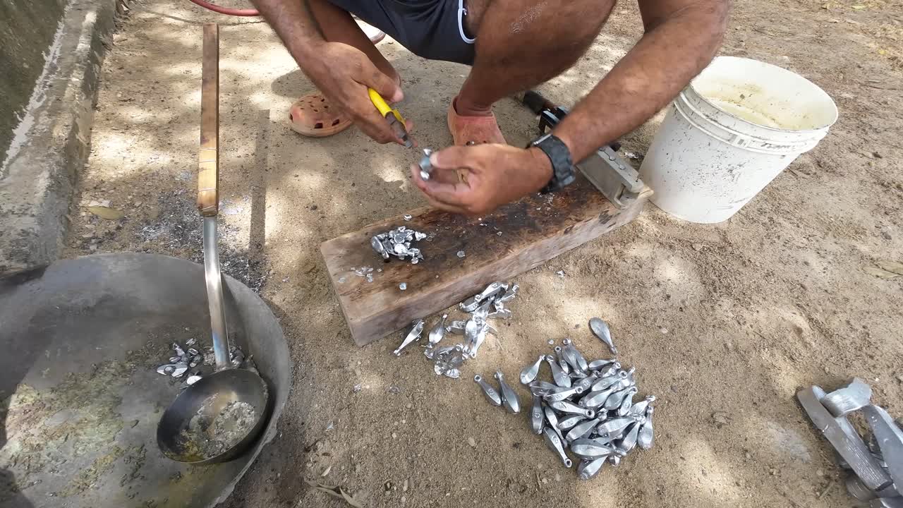 Person handcrafting fishing weights on a rustic wood block outdoors, sunlight casting shadows on the ground