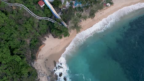 A-bird's-eye-view-of-Coral-Beach,-clear-sandy-shores-and-deep-blue-waters-with-powerful-waves