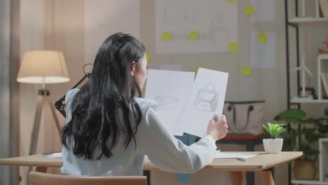 아시아 여성 디자이너가 손 가방을 바라보며 레이아웃을 스케치하는 모습
