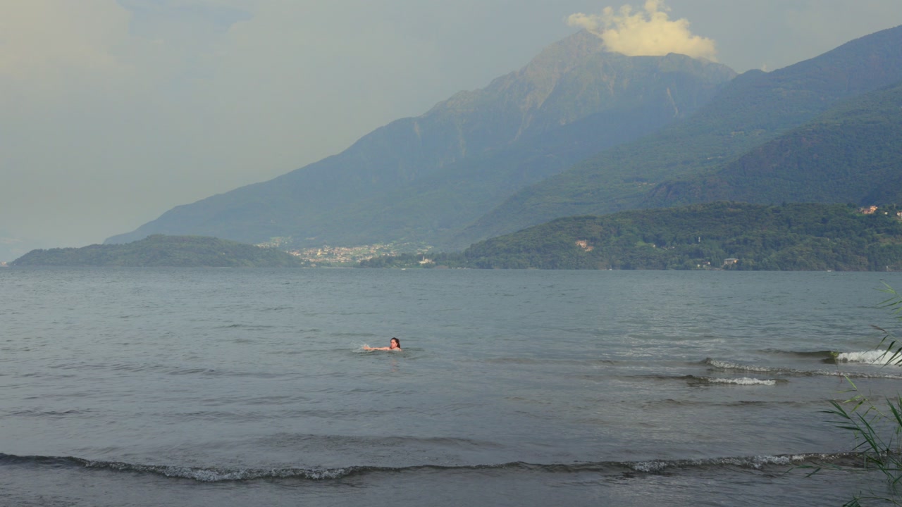 Woman swims in calm Lake Como with mountains rising in the background.