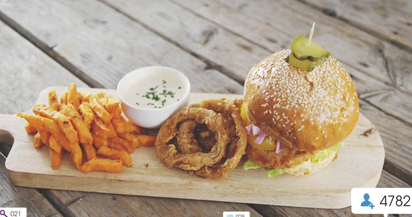 Emblemas de UI flutuantes crescendo ao redor de um hambúrguer de gergelim, anéis de cebola e batatas fritas em uma tábua de madeira, mostrando crescimento.