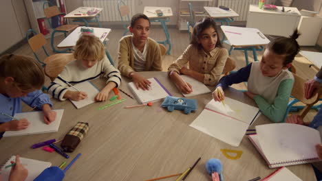 niños estudiando en la mesa redonda en la clase. el maestro hablando con los estudiantes