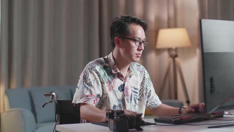 un hombre asiático en silla de ruedas está usando un escritorio junto a la cámara editando el video en casa