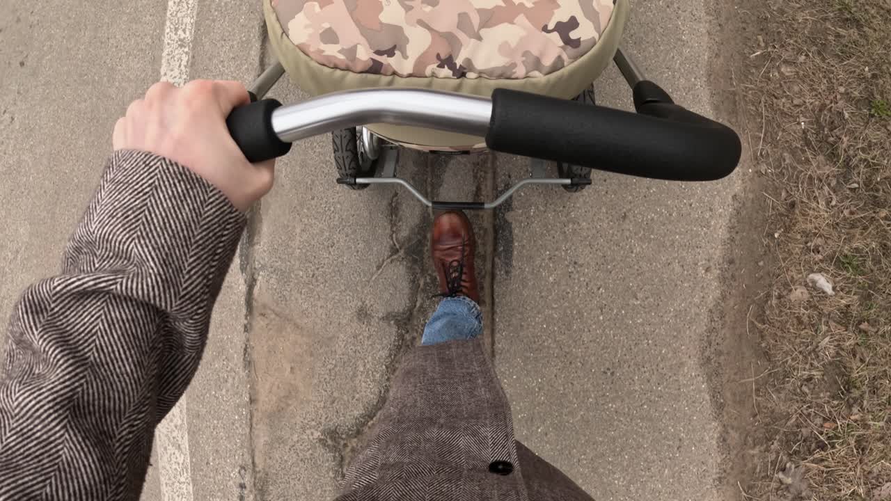 A slow top-down view shows only the kinderwagon handle and legs of a person walking, capturing subtle peaceful motion.