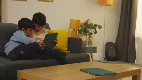 two young boys sitting on sofa at home playing games or streaming onto digital tablet together 3