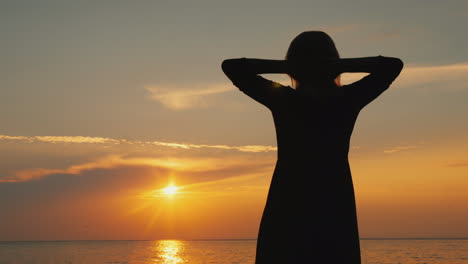 a woman admires the beautiful sky where the sun sets stands near the sea