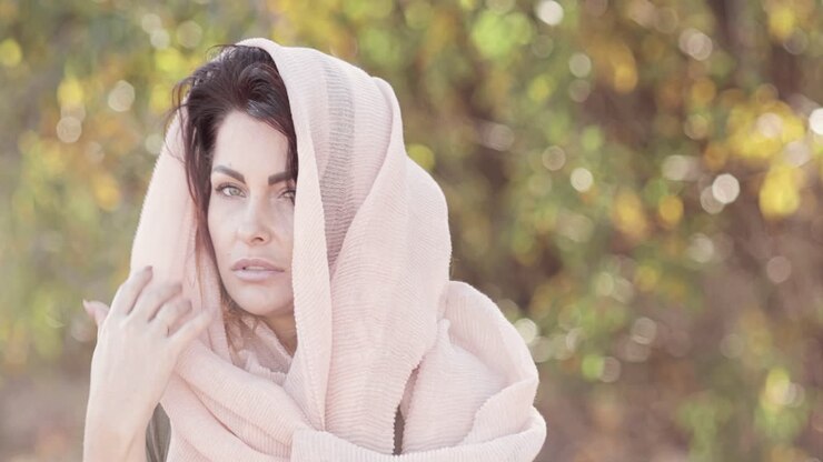 Una bella modella bruna posa con una sciarpa leggera in testa all'aperto.