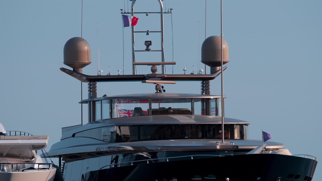 Cannes, France - October 12, 2025: Front view of a luxury superyacht with antennas, radars, and flags waving under a clear blue sky