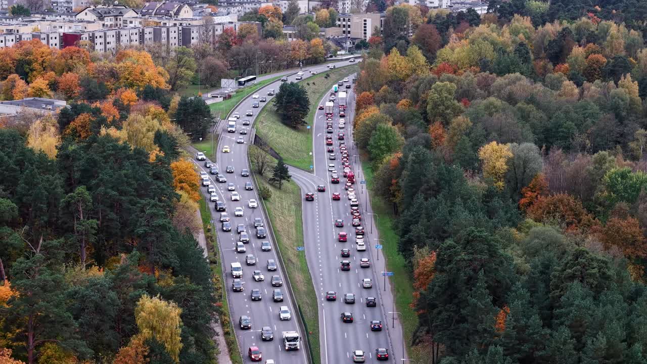 Drone panorerer fra venstre mod højre over trafikerede flersporede veje i Vilnius, der afslører tæt trafik omgivet af tæt efterårsskov