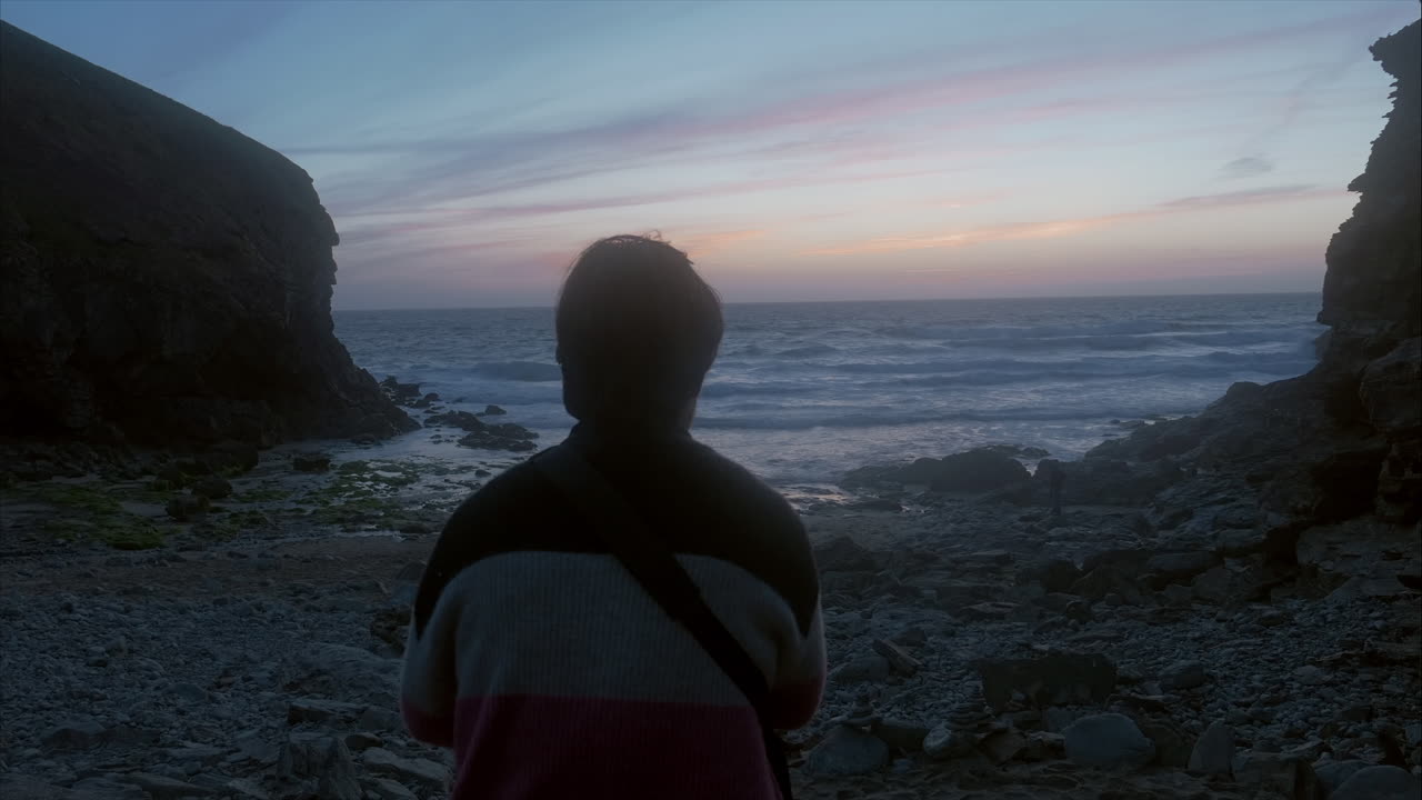 Man reflecting on life looking out at sea, and sky with blue, red and golden colours, wide shot