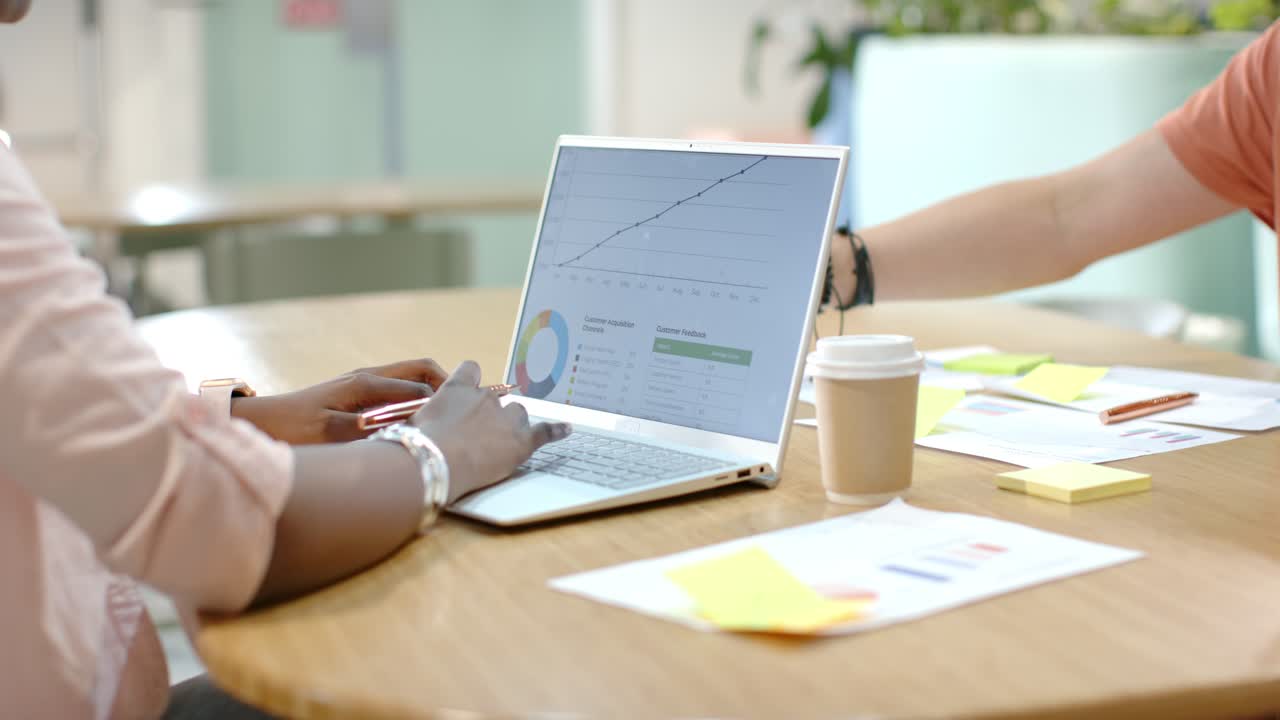 African American team working at office table when coworker with coffee, reviewing laptop charts