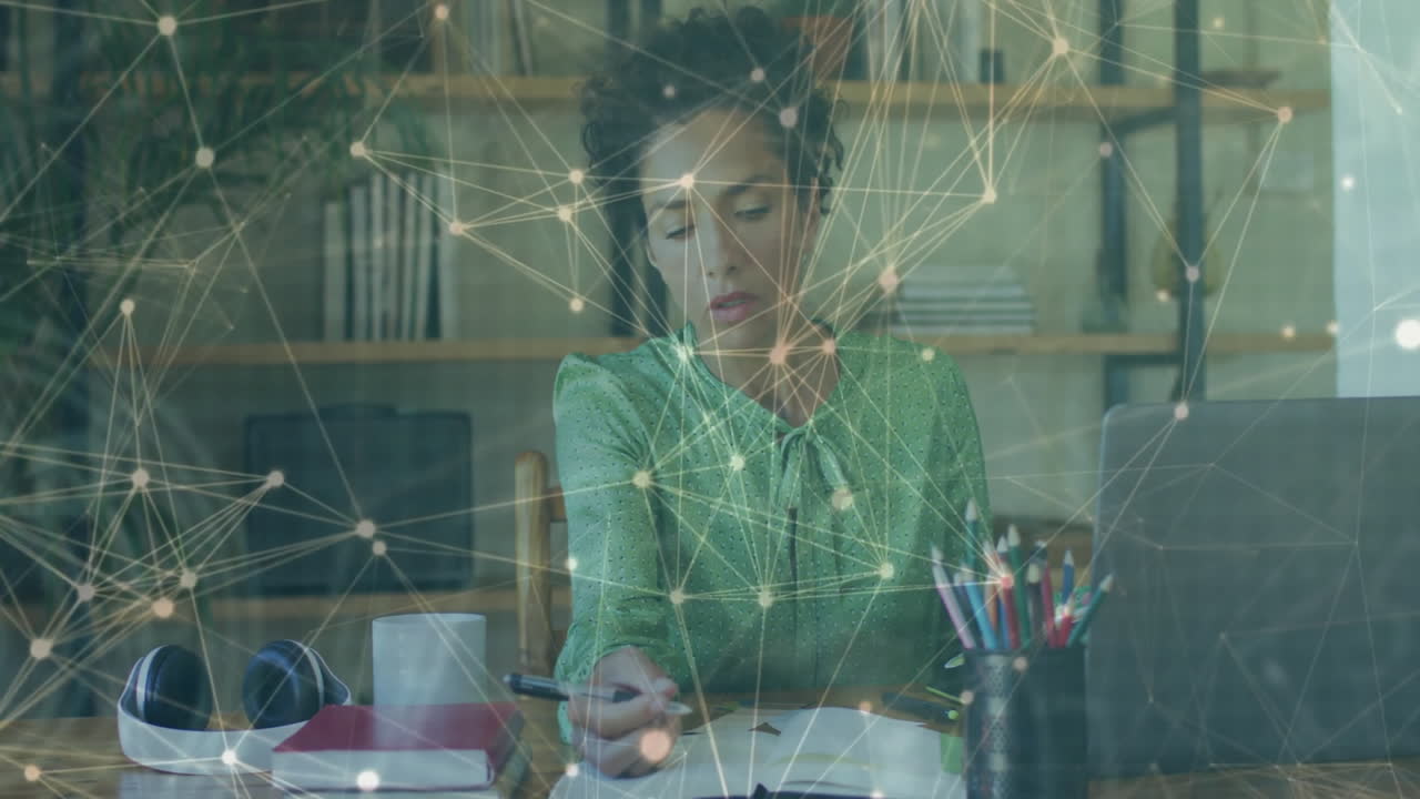 Mature woman writing in notebook at desk with laptop and pencils, displaying tech network overlay
