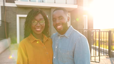 Portrait-of-happy-African-American-young-just-married-couple-standing-at-yard-of-house,-hugging-and-smiling-to-camera