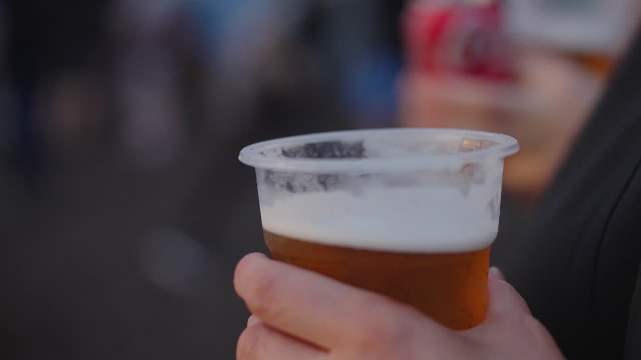 Plastic glass containing beer being held by person. Alcohol and young people