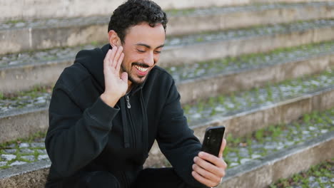 Young-Arabic-man-with-dark-curly-hair-and-beard-in-black-hoodie-sitting-on-stairs-outside