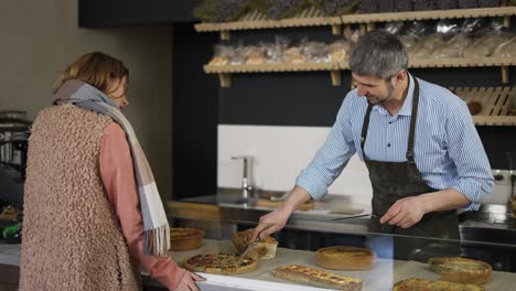 Happy-bakery-salesman-cuts-a-piece-of-cake-for-a-female-customer-and-they-have-a-casual-conversation