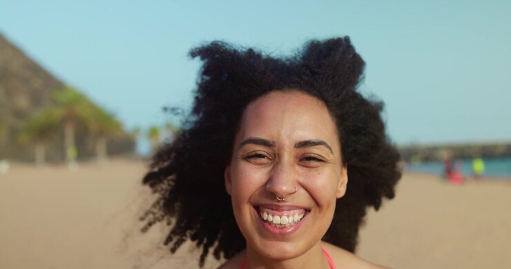 Jeune femme joyeuse aux cheveux bouclés riant sur une plage ensoleillée