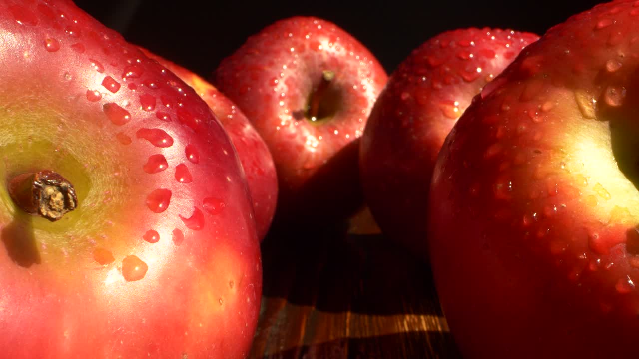 primer plano de frutas de manzana rojas con gotas de agua en una mesa de madera sobre un fondo negro
