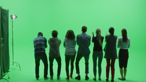 green screen chroma key studio: diverse row of seven fans cheering, jumping and applauding with hands in the air at the public sport event, concert, festival, party. back view full shot. slow motion