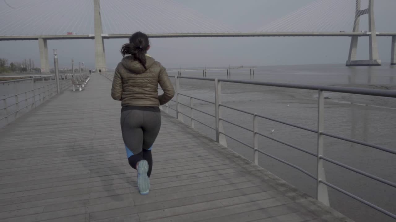 vista de atrás de una mujer joven corriendo en un muelle de madera