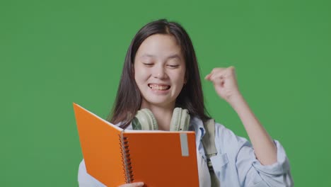 close up of asian teen girl student with a backpack reading book and screaming goal celebrating succeed learning in the green screen background studio