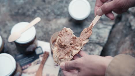 A rustic outdoor breakfast is prepared with bread, wooden tools, and jam jars