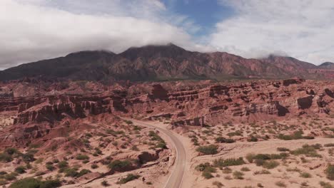 Drone-footage-of-Canchaquí-Valley,-Salta-Argentina,-exposing-the-beautiful-rock-formation-and-the-green-hills-in-the-horizon-with-the-road-in-the-middle