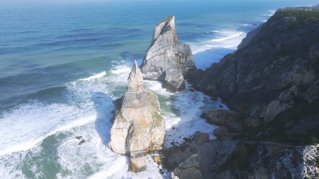 Clear morning aerial shot of Praia da Ursa by Cabo da Roca, Portugal, with blue skies and gentle waves.