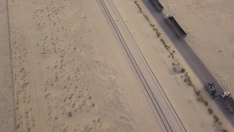 reveal a long line of trucks in the desert with sand dunes and small bushes