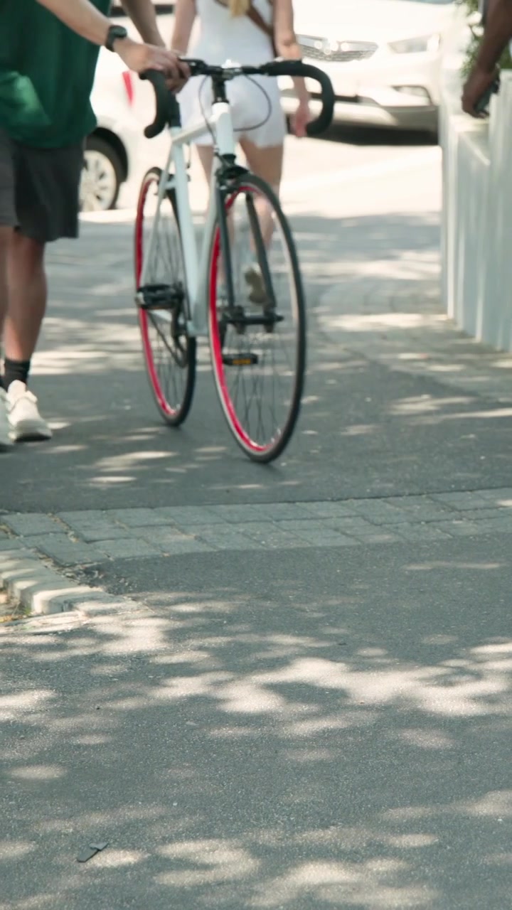 Vídeo vertical: Adulto caminhando de blusa verde e shorts preto verificando o telefone em direção à lente em caminho sombrio