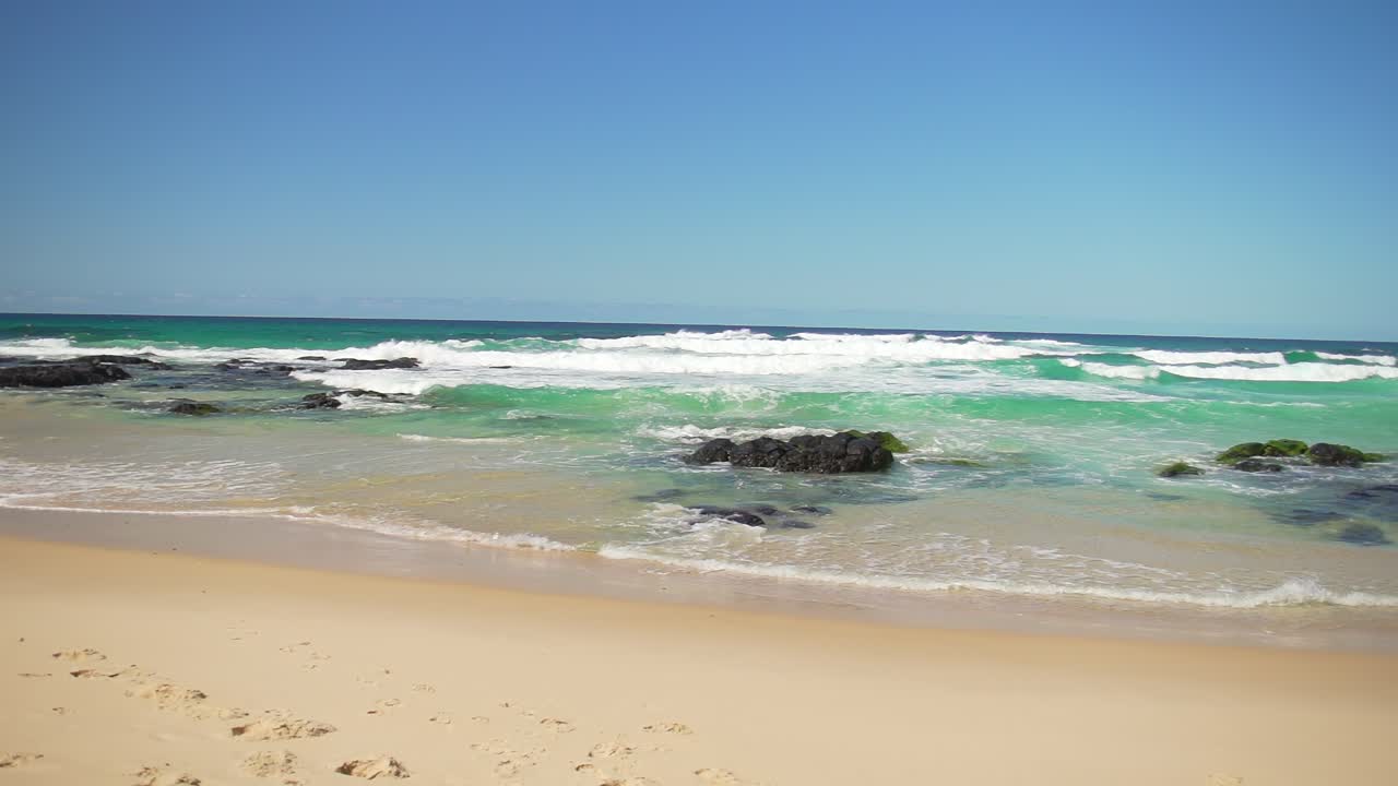 Wide shot of Cabarita Beach in Northern New South Wales, showcasing the pristine aqua waters and waves crashing over rocky sections. A perfect view of the unspoiled coastline and natural beauty.
