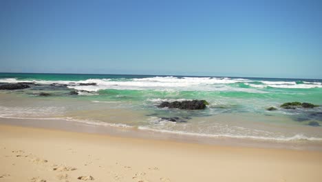 wide shot of cabarita beach in northern new south wales, showcasing the pristine aqua waters and waves crashing over rocky sections. a perfect view of the unspoiled coastline and natural beauty.