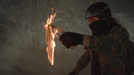 a protester, face covered and wearing a helmet, lights and throws a molotov cocktail