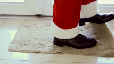 santa está entrando en la casa y sacudiendo sus zapatos en la alfombra pequeña