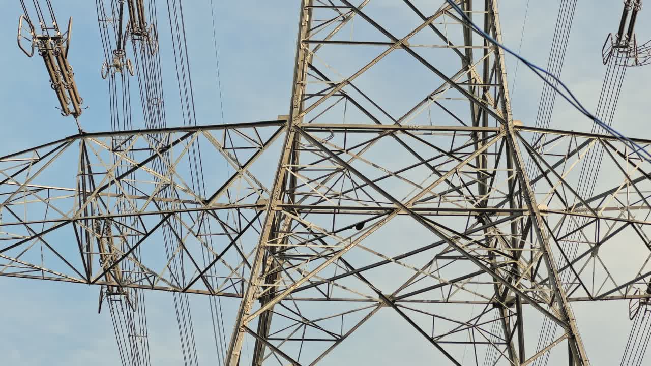 Tilt-up view capturing the full height of a lattice steel transmission tower, from base bracing to crossarms and conductors, against clear sky showing scale and structure