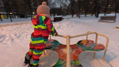 happy little girl on roundabout on the playground winter fun