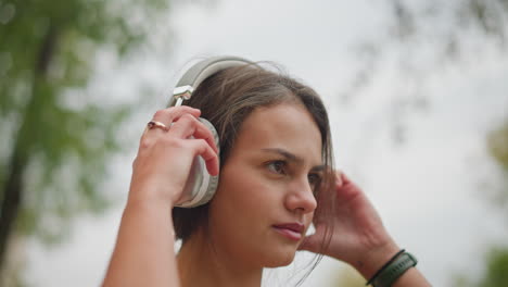 close-up view of beautiful young lady wearing headphones on her head outdoors, with a calm and focused expression, enjoying her time with music, highlighting her natural beauty