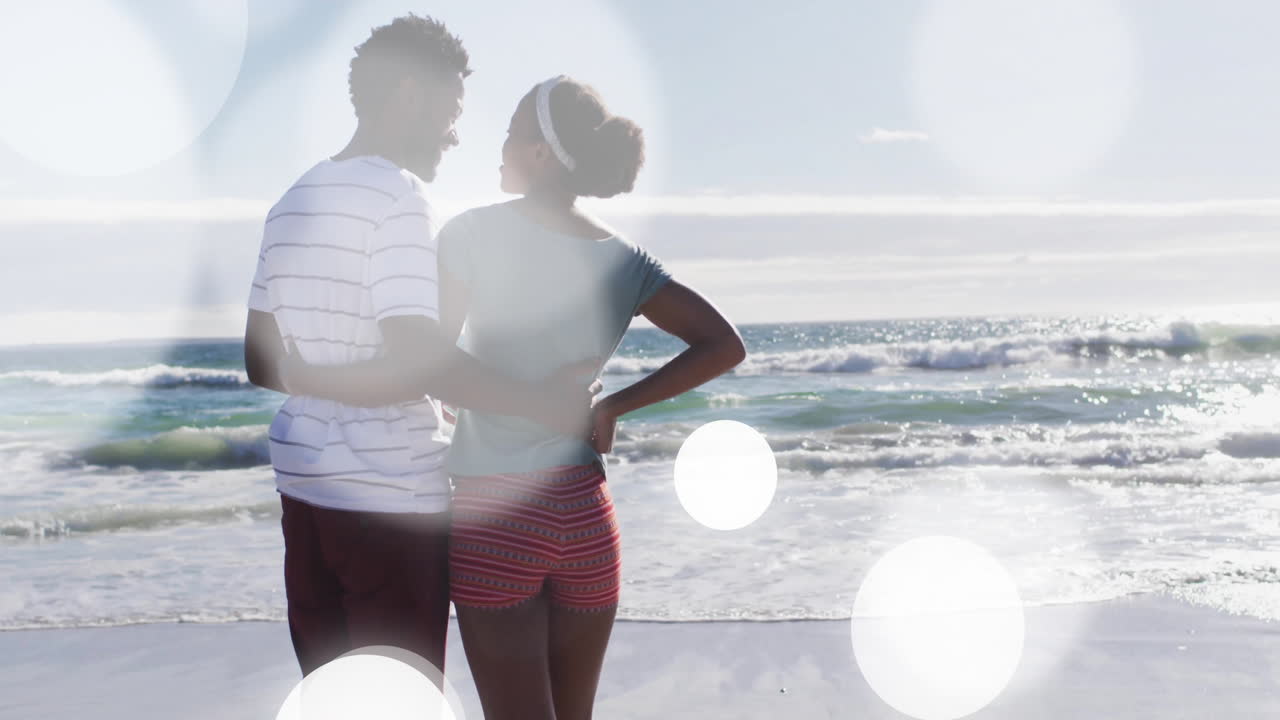 couple standing beach watching ocean under lens flare, with animated marketing graphs