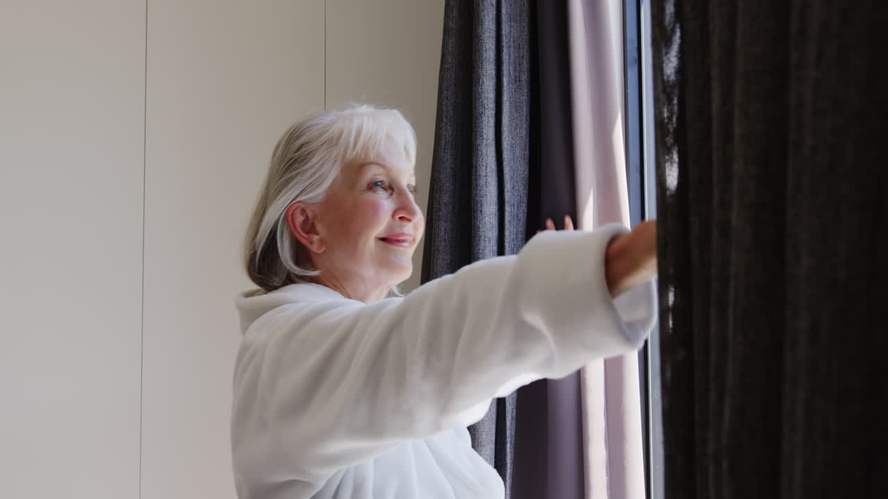 Senior woman opening curtains at home, embracing morning light with joy