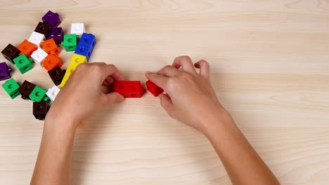 hands assembling red cubes on a wooden table