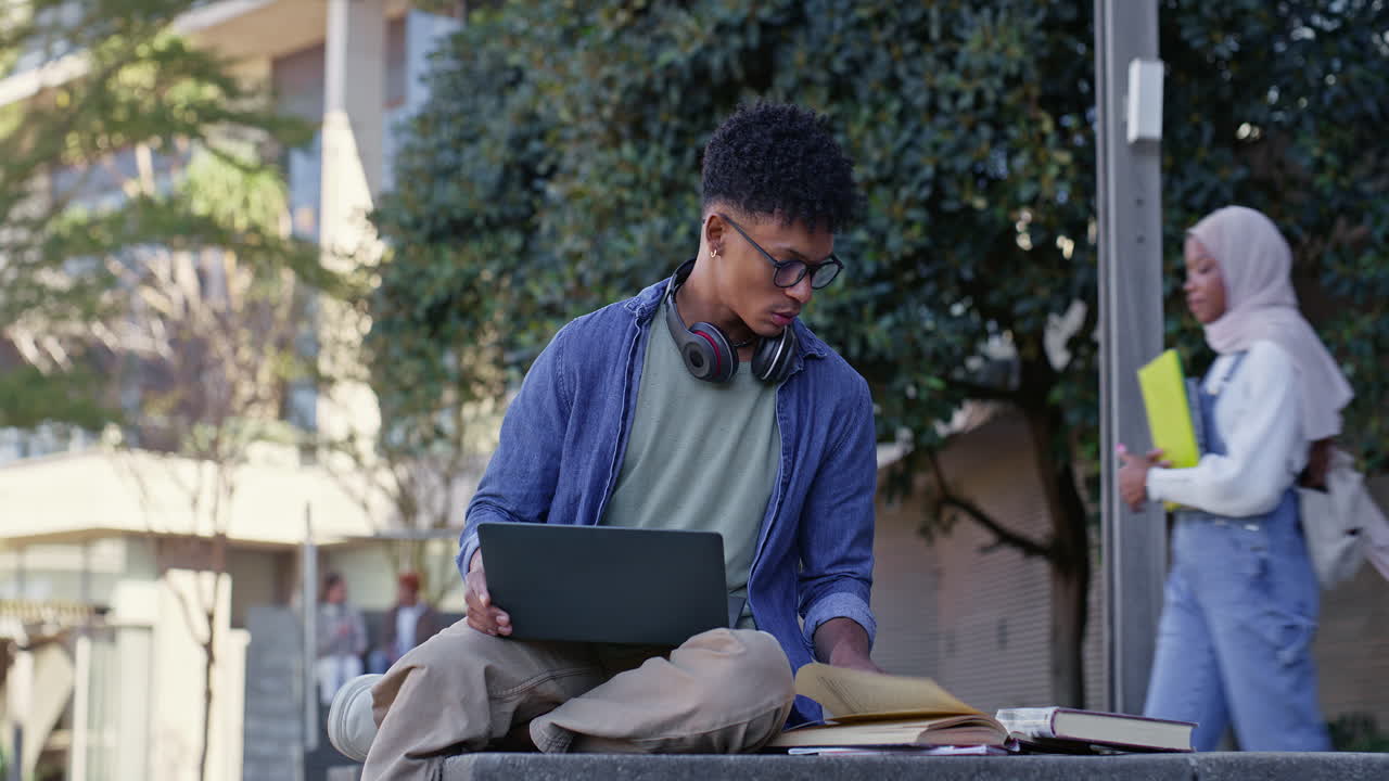 College student studying outdoors on campus with laptop and books