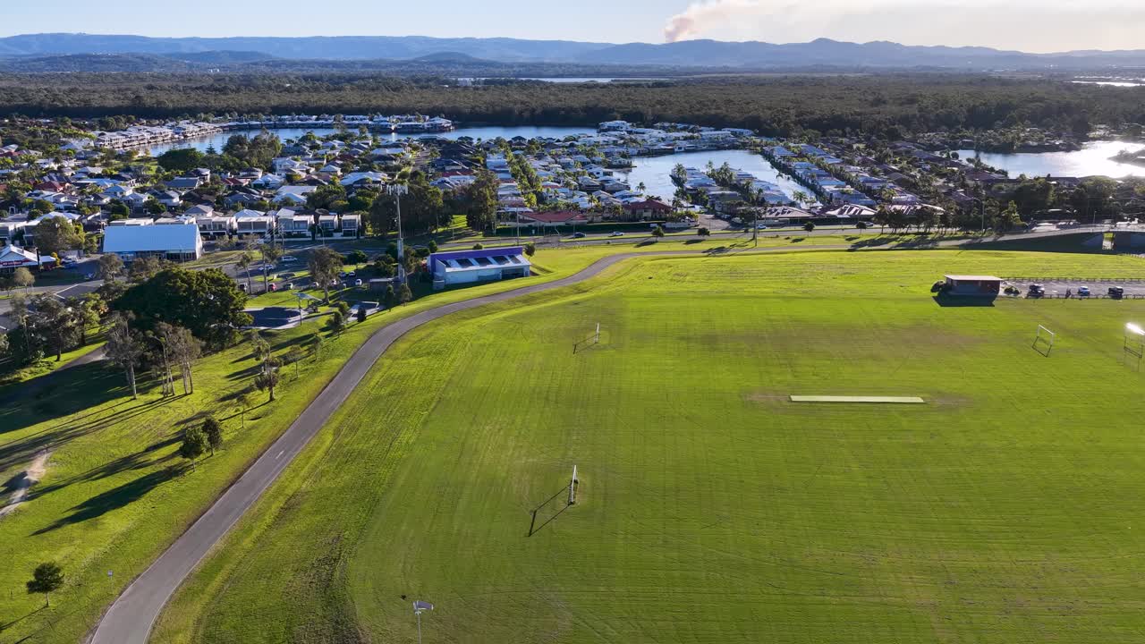 Drone footage captures a vast sports field in Gold Coast, Australia, under clear skies with surrounding urban landscape