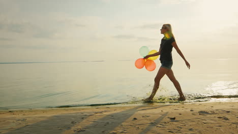 carefree young woman walks along the beach in the beautiful sky is holding balloons slow motion vide