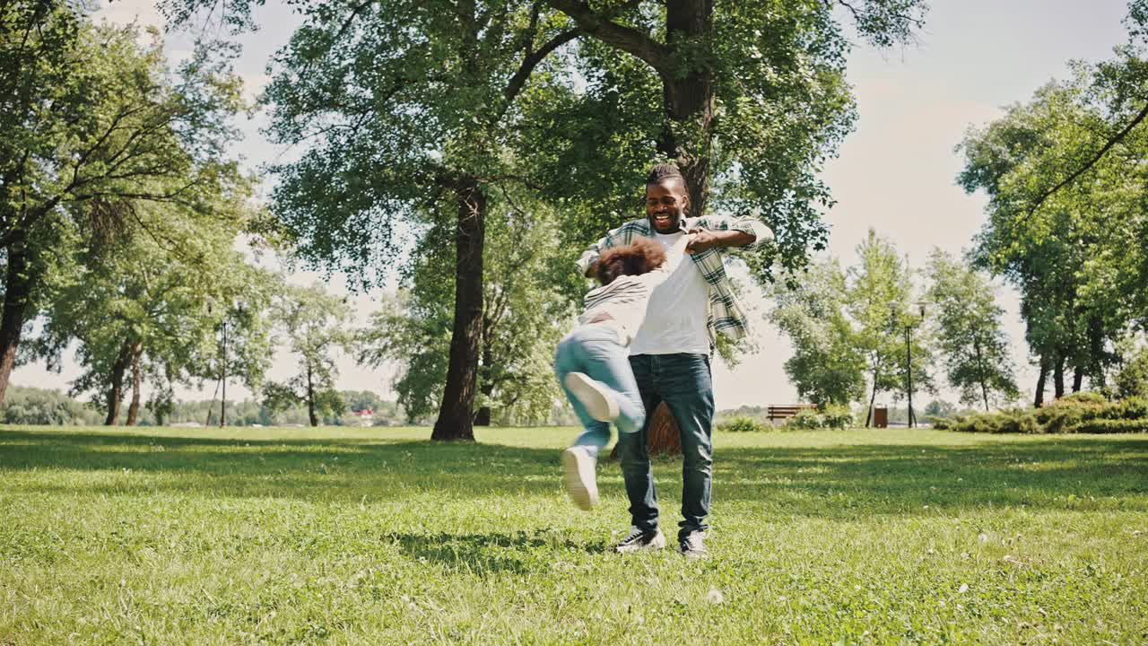 padre joven feliz gira su hija pequeña mientras camina en el parque. padre afroamericano pasando el fin de semana con su hija, concepto de día del padre