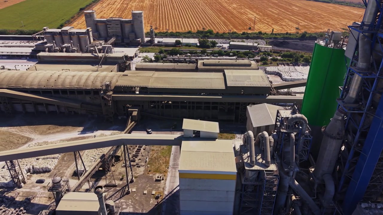 Sito industriale con campi e unità di stoccaggio sullo sfondo.