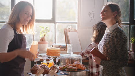 Glückliche-Barista-Frau,-Die-Kunden-Bedient,-Die-Essen-In-Einem-Belebten-Café-Kaufen,-Und-Dabei-Einen-Freundlichen-Service-Genießt