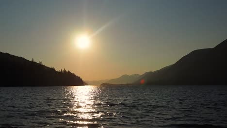 Puesta-De-Sol-En-Un-Lago-Con-Montañas-En-El-Fondo-Con-Un-Chico-Saltando-En-El-Agua-En-Silueta